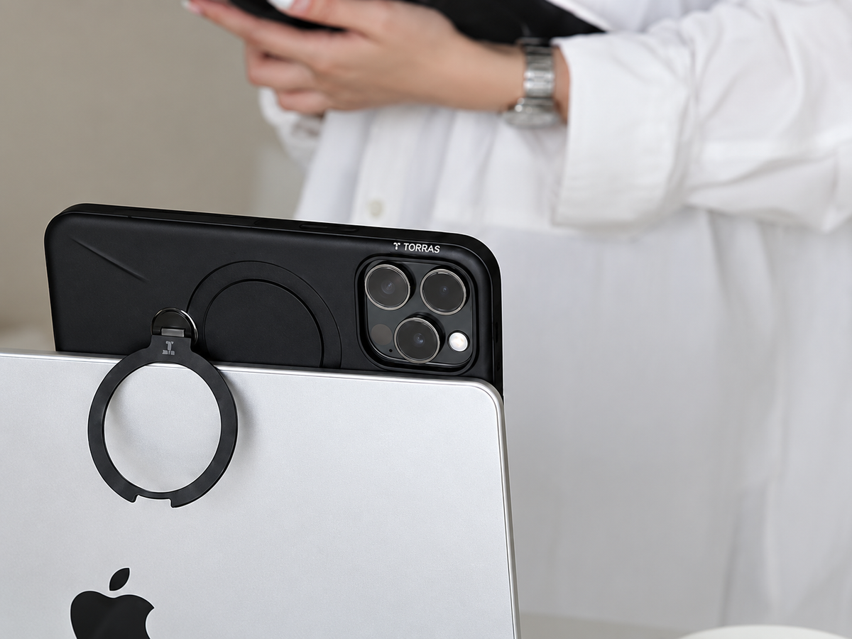 Hände halten eine schwarze iPhone-Hülle mit Ringständer vor einem MacBook