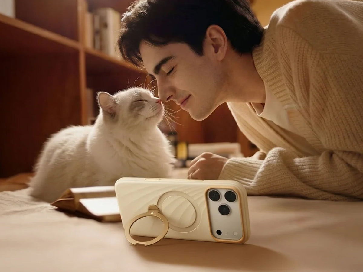 Junger Mann bei einer weißen Katze auf dem Sofa, daneben beige Hülle mit Ringständer